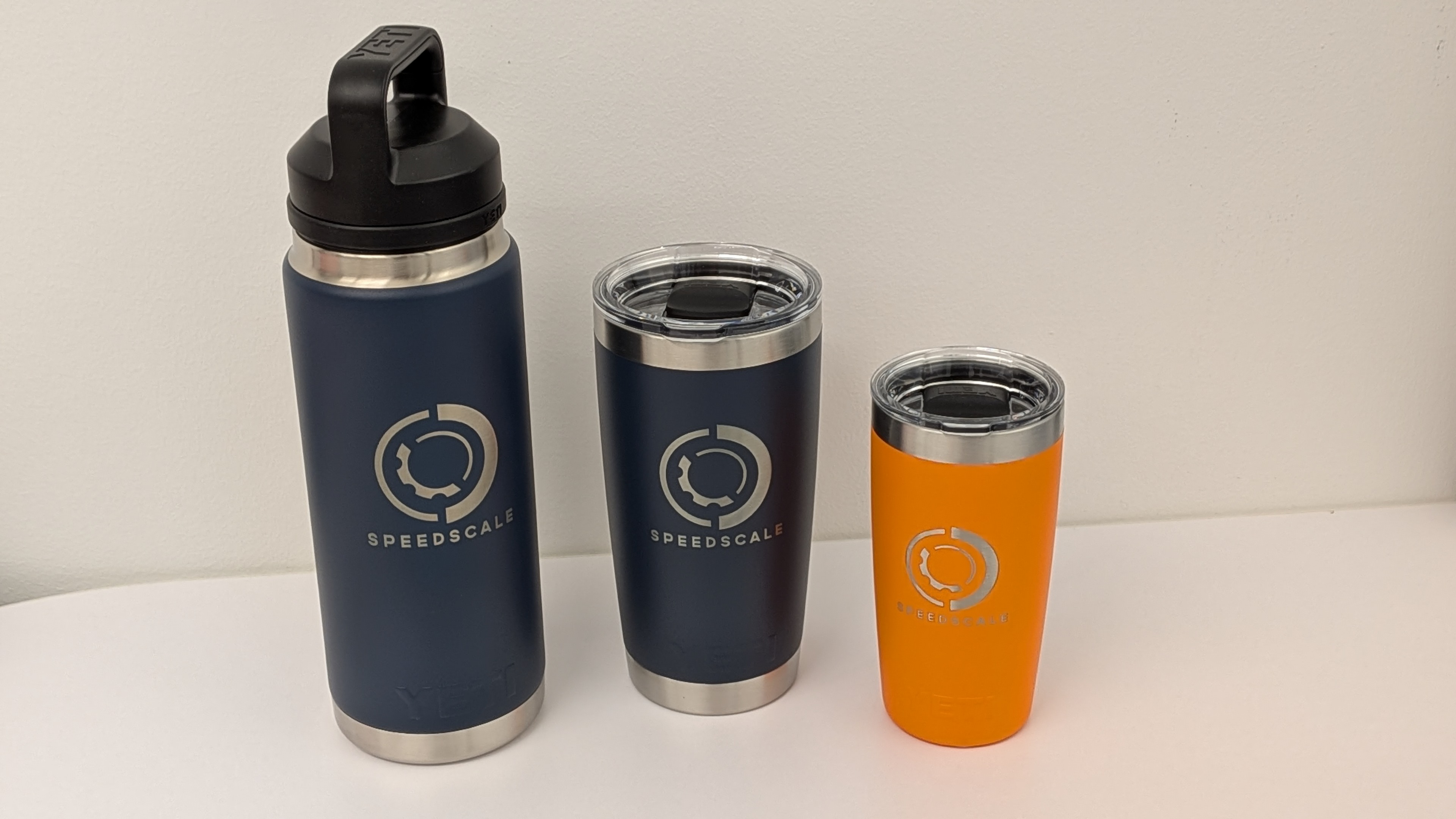 Speedscale-branded Yeti drinkware in navy and orange lined up on a table.